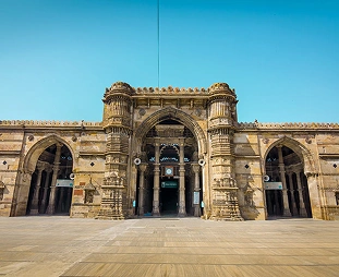 Front view of a large sandstone triumphal gate with a central arched entrance and two side arches, ornate facade, under a bright blue sky.