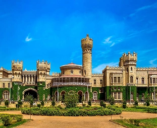 Castle-like building with a tall central tower, battlements, arches, ivy-covered walls, and a manicured garden against a bright blue sky.