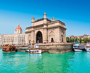 Gateway of India arch on the waterfront with turquoise water and boats in the foreground.
